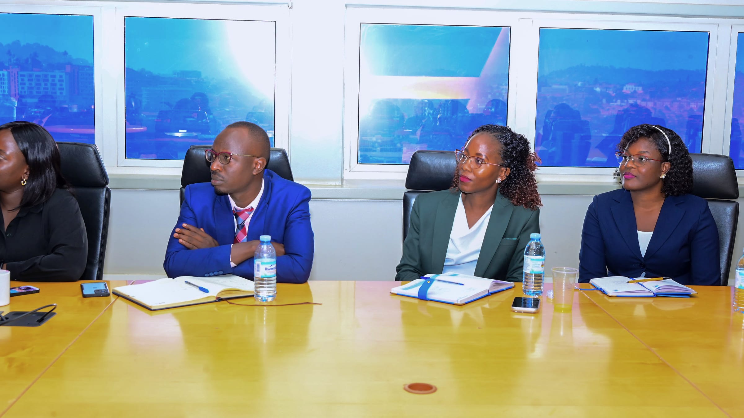 Apio and three colleagues seated at a boardroom table taking notes, with the city visible through the windows behind them