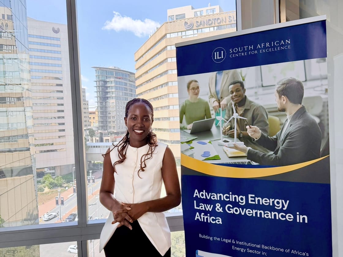 Apio beside a banner for a programme on advancing energy law and governance in Africa, with the Sandton skyline behind her